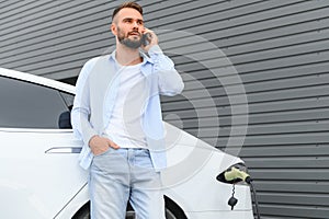 Happy man using smart phone and charging car at vehicle charging station