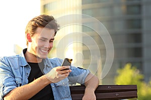 Happy man using smart phone sitting on a bench