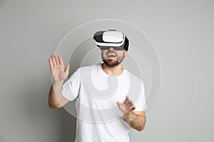 Happy man using virtual reality headset on light grey background