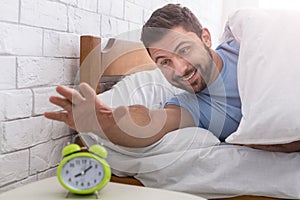 Happy man waking up and stopping alarm clock