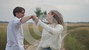 Happy man walking with woman outdoors spinning spouse holding hands in slow motion. Portrait of handsome Caucasian