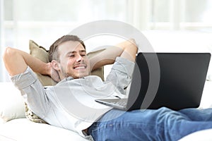 Happy man watching movie on laptop lying on a couch
