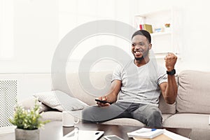 Happy man watching tv using remote controller in living room