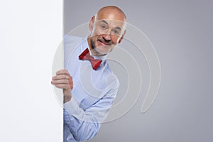 Happy man wearing bow tie while looking out of white board while standing at isolated background