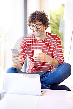 Happy man wearing casual clothes while text messaging and drinking tea at home