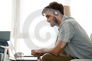 Happy man wearing headset study online on laptop making notes photo