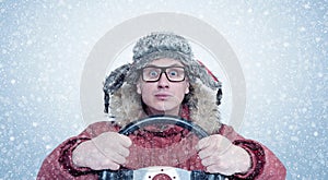 Happy man in winter clothes with a steering wheel, snow blizzard. Concept car driver