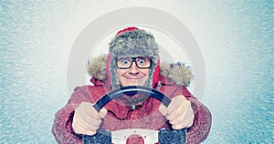 Happy Man in winter clothes with a steering wheel, snow blizzard. Concept car driver