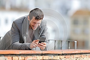 Happy man in winter using mobile phone in a balcony