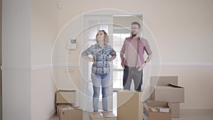 Happy man and woman in casual dress with boxes in hands standing in room. Married couple moves into a new home.