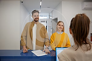 Happy man and woman couple signing document at modern clinic reception desk