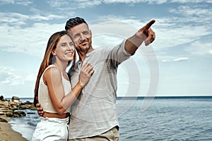 Happy man and woman couple walking on the beach and man pointing at something