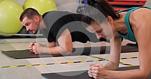 Happy man and woman doing plank exercise on carpet in gym club. Fitnes couple practicing plank workout together in