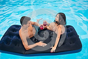 Happy man and woman drinking cocktails on a mattress in the pool enjoying each other and a holiday, top view