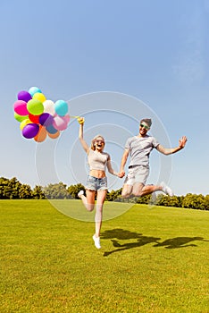 Happy man and woman holding balloons and jumping in the park