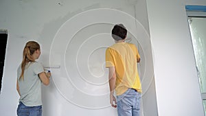 A happy man and woman paint the wall using a roller painter. They are renovating their apartment. DIY home renovation