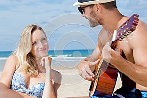 happy man and woman playing guitar on beach