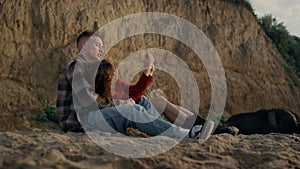 Happy man and woman relaxing on beach. Cheerful girl taking photo on smartphone