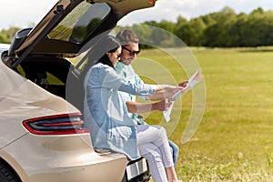 Happy man and woman with road map at hatchback car