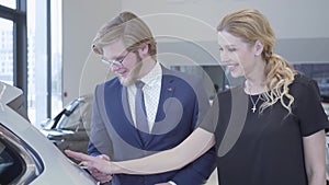 Happy man and woman between rows of new electric cars in motor show choosing one to buy. Couple hugging, around many