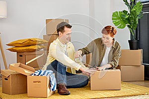 Happy man and woman seal wrap packages boxes with tape dispenser relocate to new house