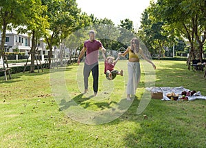 A happy man and woman stroll hand-in-hand in the sunlit park, their small child toddling happily between them