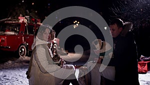 Happy man and woman together pets sitting on winter picnic on New Year car background at winter night. Couple relaxing