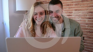 Happy man and woman using computer together while sitting in the living room. Young smiling couple connected on internet