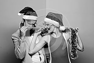 Happy man and woman wear santa hats and funny sunglasses. Cheerful couple celebrate new year. Corporate holiday party