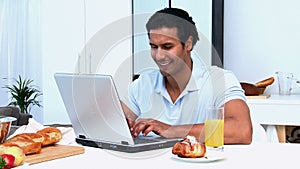 Happy man working on the laptop while having breakfast