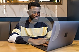 Happy man writing text on laptop in a modern coffee shop. Happy african student surfing the web on laptop with wifi free