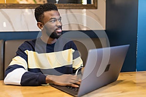 Happy man writing text on laptop in a modern coffee shop. Happy african student surfing the web on laptop with wifi free