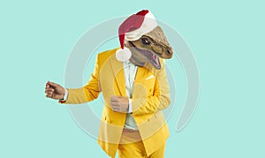Happy man in a yellow suit, dinosaur mask and Christmas hat dancing on a turquoise background