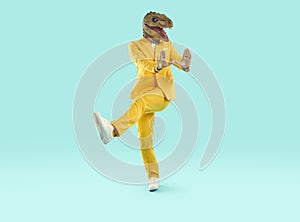 Happy man in a yellow suit and a funny dinosaur mask dancing on a blue studio background