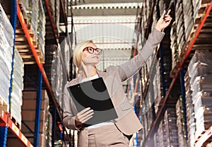 Happy manager holding clipboard in warehouse with lots of products, low angle view