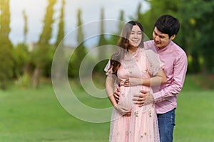 Happy married couple is expecting a baby. man embraces his pregnant wife in park
