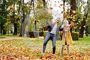 Happy married Couple having fun together outdoor in the golden autumn park, throwing leaves and laughing. Wife and husband in love