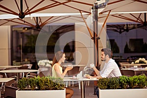 Happy married couple is on a honey moon, having brunch in nice cafe with modern interior, light summer terrace with green nice pla