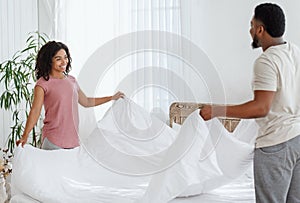 Happy married couple making bed together in the morning