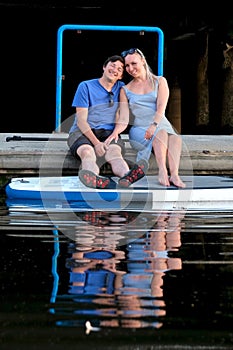 Happy married couple in marina with paddle board floating on water.