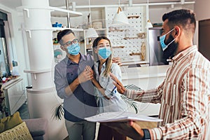 Happy married couple in medical masks standing in the new house with male real-estate agent. Pandemic concept