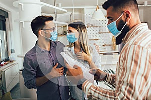 Happy married couple in medical masks standing in the new house with male real-estate agent. Pandemic concept