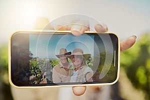 Happy married senior couple taking selfies on cellphone in vineyard. Smiling Caucasian husband and wife standing