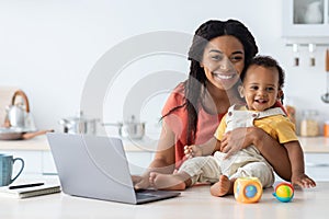 Happy Maternity Leave. Black Lady Working On Laptop With Baby In Kitchen