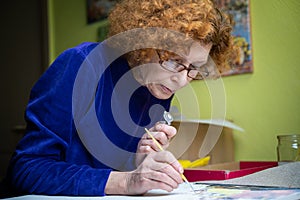Happy mature artist woman painting on canvas at home studio. Express creativity. Positive elderly woman holding brush and drawing