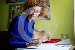 Happy mature artist woman painting on canvas at home studio. Express creativity. Positive elderly woman holding brush and drawing