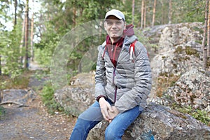 Happy mature backpacker resting on a stone at the footpath in the rocky forest