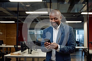 Happy mature black man in businesswear using mobile phone in office photo