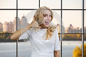 Happy mature blonde businesswoman shows call me gesture sign.