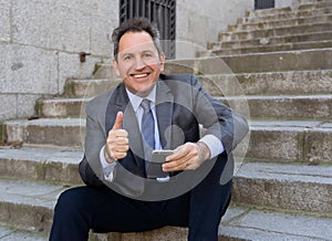 Happy mature business entrepreneur man sitting outdoors urban stairs working and using smart phone